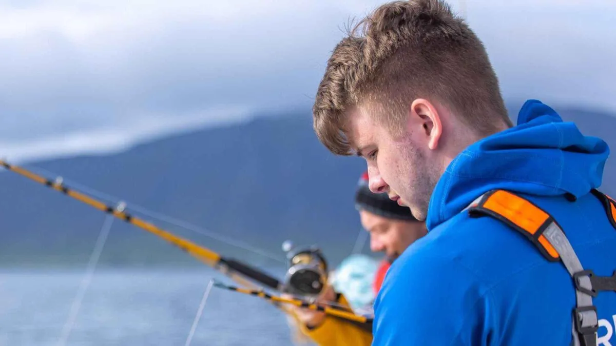 Anglers holding rods over the rail of a fishing boat in Faxaflói Bay on a sea fishing tour from Reykjavik, Iceland