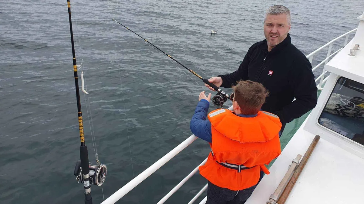 Angler reeling in a cod beside the Reykjavik coastline on the Finest Catch sea angling tour on the Jóhanna, a fishing tour in Iceland
