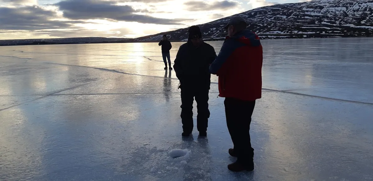 Angler jigging through a hole in the ice on frozen Ljósavatn lake on an ice fishing tour from Akureyri, Iceland